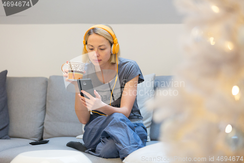 Image of Young cheerful woman sitting indoors at home living room sofa using social media on phone for video chatting and staying connected with her loved ones. Stay at home, social distancing lifestyle