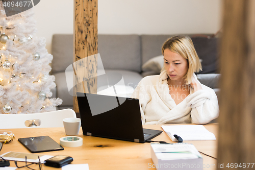 Image of Young female entrepreneur wearing cosy warm bathrobe working remotly from home in winter Christmas time during 2020 corona virus pandemic. Work from home, selter in place, concept.