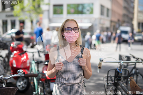 Image of Portrait of casual yound woman walking on the street wearing protective mask as protection against covid-19 virus. Incidental people on the background