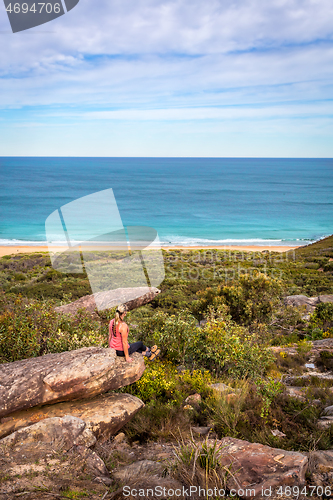 Image of Female sitting on rocks in active wear with views out to beach a