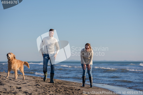 Image of couple with dog having fun on beach on autmun day