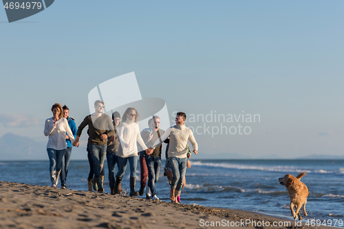 Image of Group of friends running on beach during autumn day