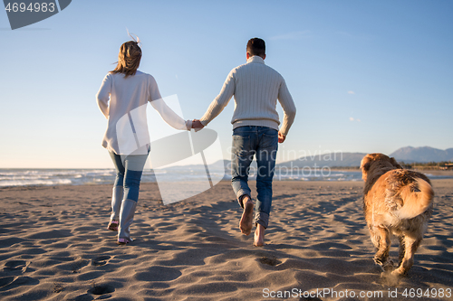 Image of couple with dog having fun on beach on autmun day