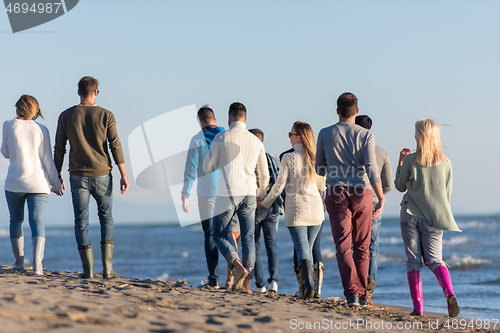 Image of Group of friends running on beach during autumn day
