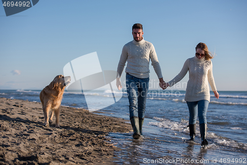 Image of couple with dog having fun on beach on autmun day