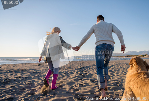 Image of couple with dog having fun on beach on autmun day