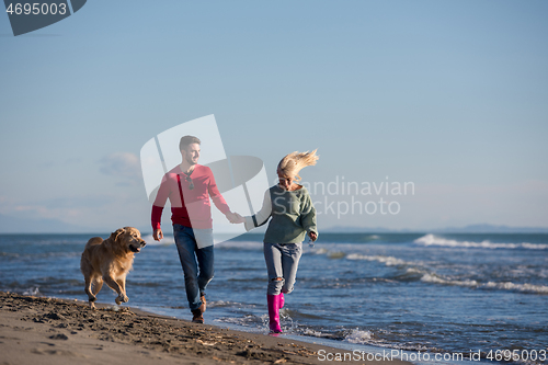 Image of couple with dog having fun on beach on autmun day