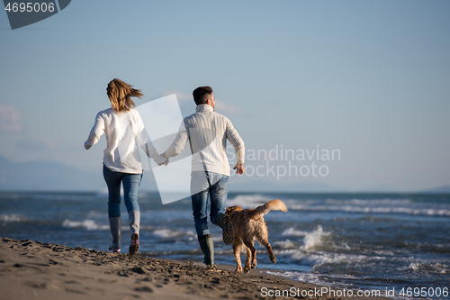 Image of couple with dog having fun on beach on autmun day