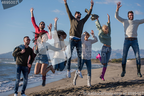 Image of young friends jumping together at autumn beach