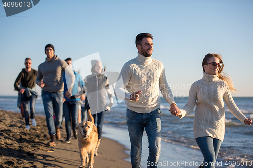 Image of Group of friends running on beach during autumn day