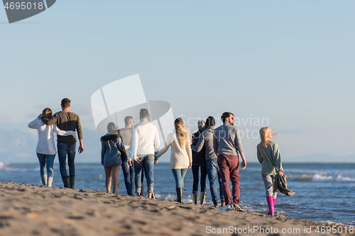 Image of Group of friends running on beach during autumn day