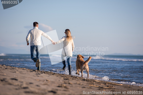 Image of couple with dog having fun on beach on autmun day