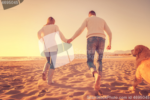 Image of couple with dog having fun on beach on autmun day