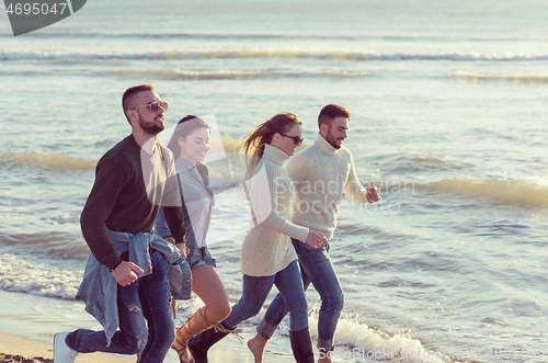 Image of Group of friends running on beach during autumn day