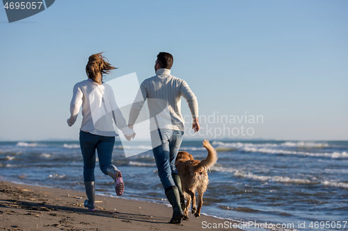 Image of couple with dog having fun on beach on autmun day