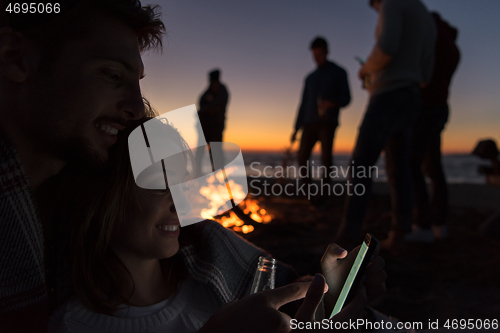 Image of Couple enjoying bonfire with friends on beach