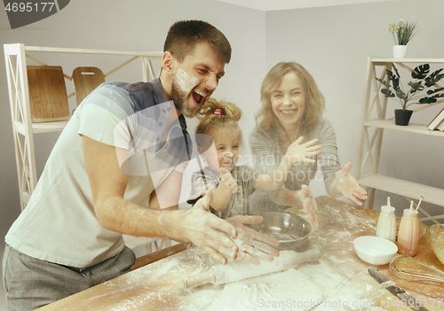 Image of Cute little girl and her beautiful parents preparing the dough for the cake in kitchen at home