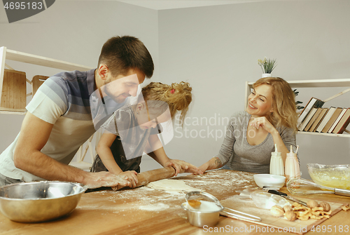 Image of Cute little girl and her beautiful parents preparing the dough for the cake in kitchen at home