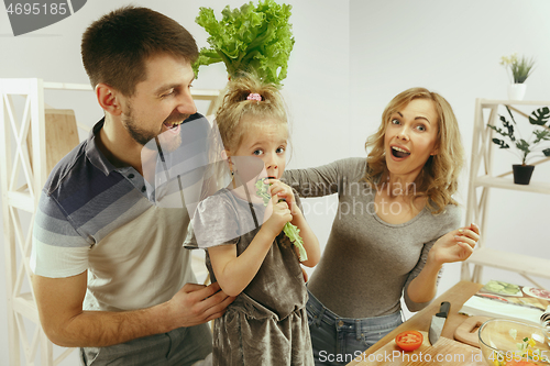 Image of Cute little girl and her beautiful parents are cutting vegetables in kitchen at home