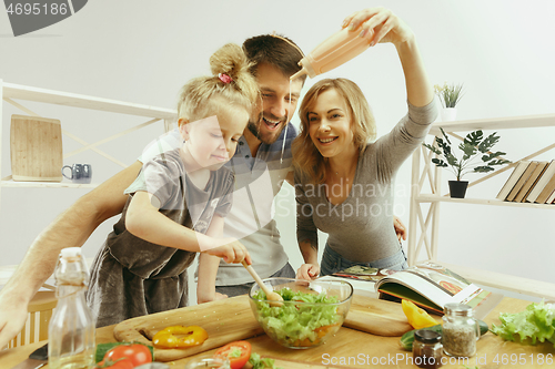 Image of Cute little girl and her beautiful parents are cutting vegetables in kitchen at home