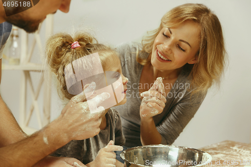 Image of Cute little girl and her beautiful parents preparing the dough for the cake in kitchen at home