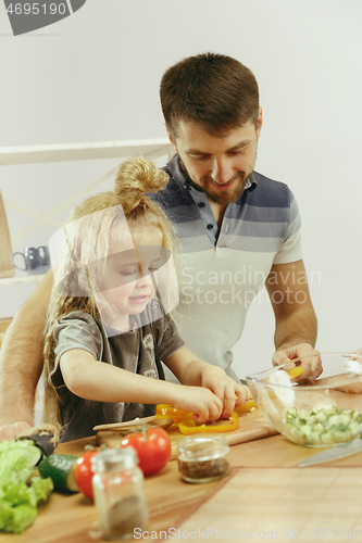 Image of Cute little girl and her beautiful parents are cutting vegetables in kitchen at home