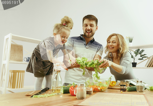 Image of Cute little girl and her beautiful parents are cutting vegetables in kitchen at home