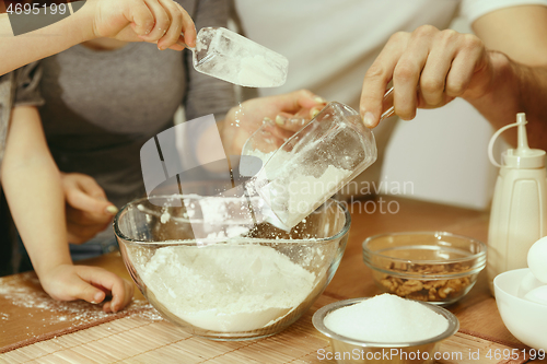 Image of Cute little girl and her beautiful parents preparing the dough for the cake in kitchen at home