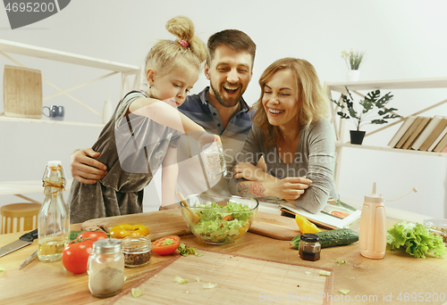 Image of Cute little girl and her beautiful parents are cutting vegetables in kitchen at home