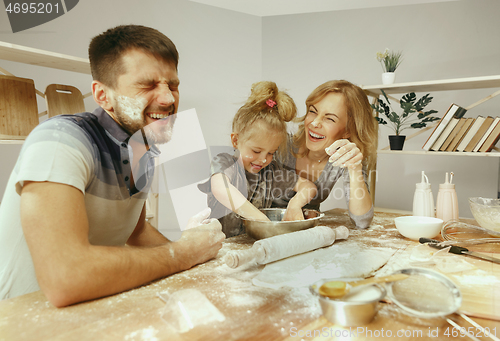 Image of Cute little girl and her beautiful parents preparing the dough for the cake in kitchen at home