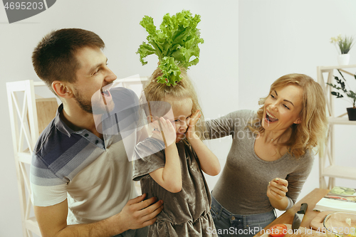 Image of Cute little girl and her beautiful parents are cutting vegetables in kitchen at home