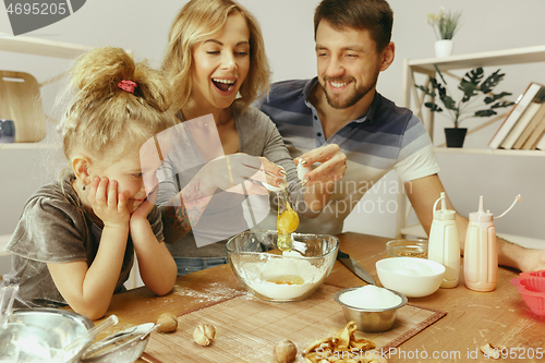 Image of Cute little girl and her beautiful parents preparing the dough for the cake in kitchen at home