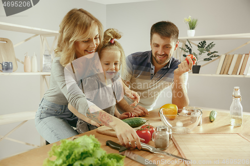 Image of Cute little girl and her beautiful parents are cutting vegetables in kitchen at home