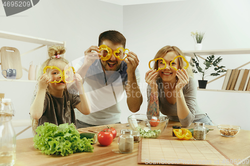 Image of Cute little girl and her beautiful parents are cutting vegetables in kitchen at home