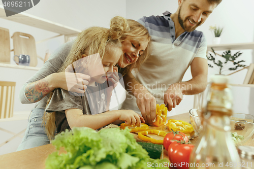 Image of Cute little girl and her beautiful parents are cutting vegetables in kitchen at home