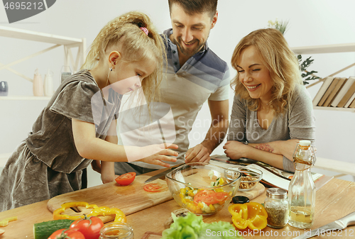 Image of Cute little girl and her beautiful parents are cutting vegetables in kitchen at home