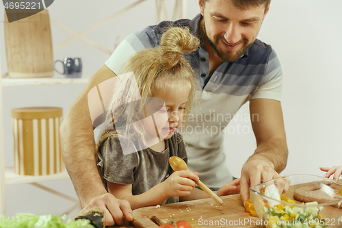 Image of Cute little girl and her beautiful parents are cutting vegetables in kitchen at home