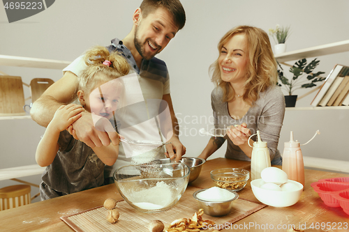 Image of Cute little girl and her beautiful parents preparing the dough for the cake in kitchen at home