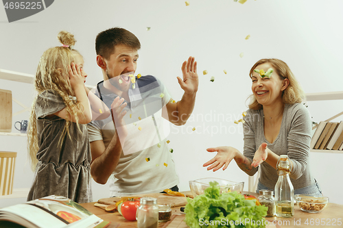 Image of Cute little girl and her beautiful parents are cutting vegetables in kitchen at home