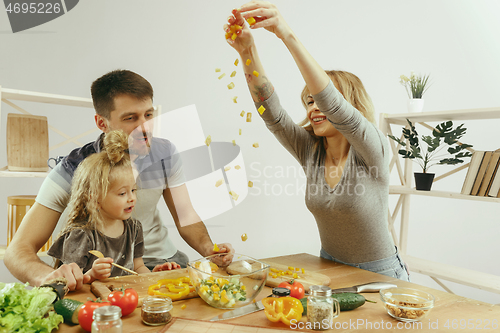 Image of Cute little girl and her beautiful parents are cutting vegetables in kitchen at home