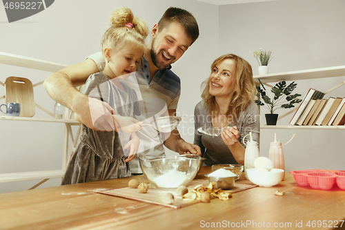 Image of Cute little girl and her beautiful parents preparing the dough for the cake in kitchen at home