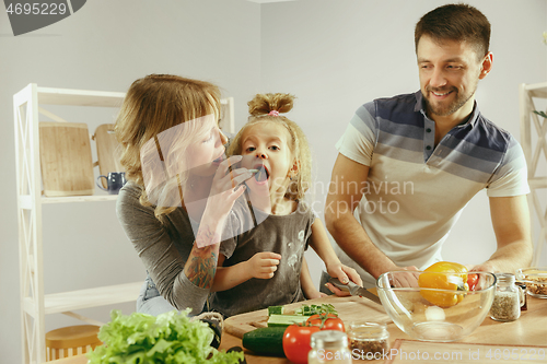 Image of Cute little girl and her beautiful parents are cutting vegetables in kitchen at home