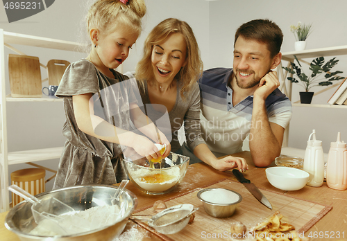 Image of Cute little girl and her beautiful parents preparing the dough for the cake in kitchen at home