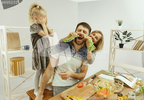 Image of Cute little girl and her beautiful parents are cutting vegetables in kitchen at home