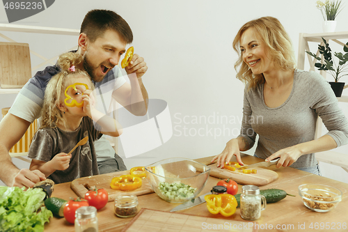 Image of Cute little girl and her beautiful parents are cutting vegetables in kitchen at home