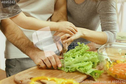 Image of Cute little girl and her beautiful parents are cutting vegetables in kitchen at home