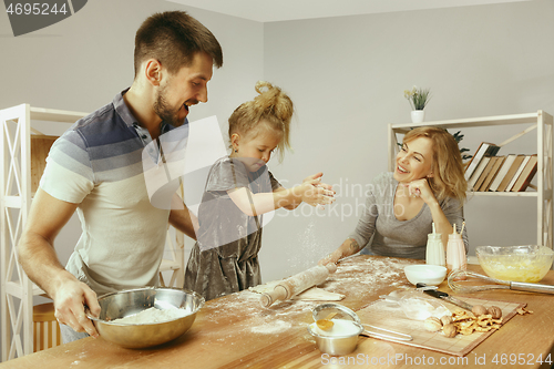 Image of Cute little girl and her beautiful parents preparing the dough for the cake in kitchen at home