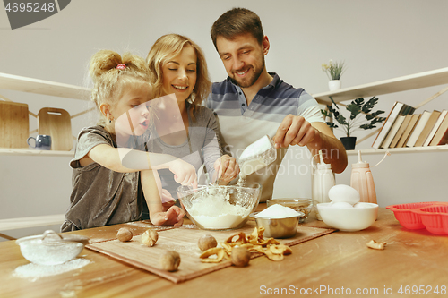 Image of Cute little girl and her beautiful parents preparing the dough for the cake in kitchen at home