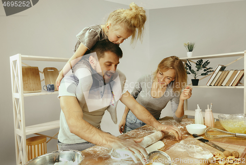 Image of Cute little girl and her beautiful parents preparing the dough for the cake in kitchen at home