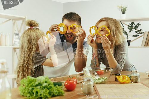 Image of Cute little girl and her beautiful parents are cutting vegetables in kitchen at home